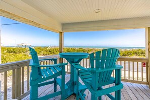 A wooden deck with a table and chairs, overlooking a beach with a clear view of the ocean. - Shoreside Cottage - Classic 2 BR Beauty - Amazing Views from Covered Porch! Dog (Surf City)