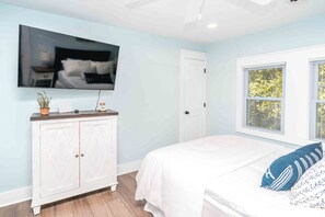 Une chambre à coucher avec un lit, un téléviseur fixé au mur, une fenêtre avec des stores et une porte.