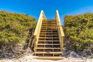 A wooden staircase leading up to a sandy area with dense green shrubbery on either side. - Shoreside Cottage - Classic 2 BR Beauty - Amazing Views from Covered Porch! Dog (Surf City)