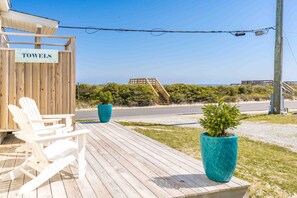 Une terrasse en bois avec deux fauteuils Adirondack, un panneau indiquant « SERVIETTES », et une vue sur la plage et l’océan.