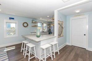 A kitchen with a central island, bar stools, a refrigerator, and a door with a sign. - Shoreside Cottage - Classic 2 BR Beauty - Amazing Views from Covered Porch! Dog (Surf City)