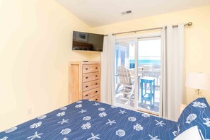 Un dormitorio con cama, cómoda, televisor y balcón con sillas.