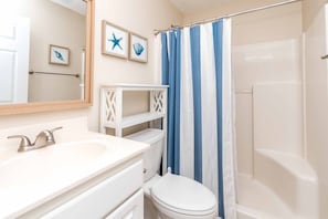 A bathroom with a white sink, a toilet, a shower with a blue and white striped curtain, and framed artwork on the wall. - Beachy Bliss - Cute 3 BR (Half Duplex) on 2nd Row with Great Views! Dog (Surf City)