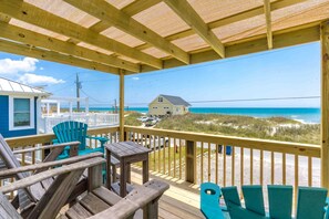A wooden deck with chairs overlooking a beach and a house.