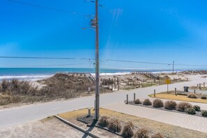 A coastal road with a pedestrian walkway, a beach in the background, and a clear sky.