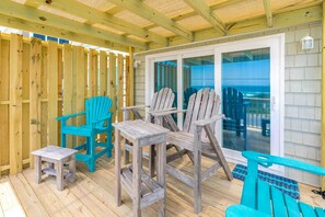 A covered outdoor seating area with wooden furniture and a view through glass doors. - Coastin' Along - Cute 3 BR (Half Duplex) with Great Views! Dog Friendly! (Surf City)