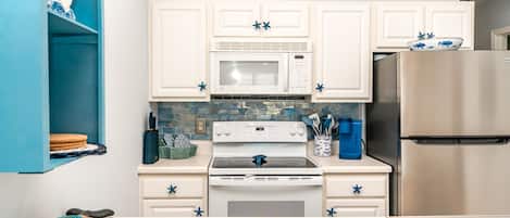 A kitchen with white cabinets, a microwave, a stove, and a refrigerator.