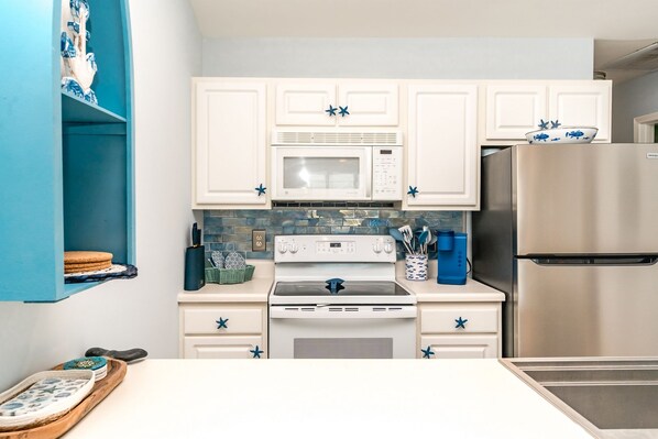 A kitchen with white cabinets, a microwave, a stove, and a refrigerator.