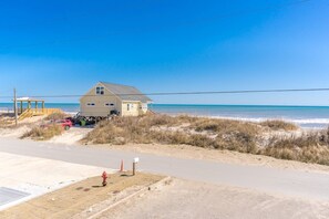 Uma casa de praia com um caminho de acesso de areia, um hidrante vermelho e vista clara do oceano.