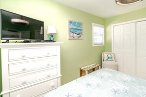 Un dormitorio con cama, cómoda, televisor, lámpara, obra de arte y una mesita.