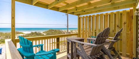 A wooden deck with a view of the beach, featuring a table and chairs.