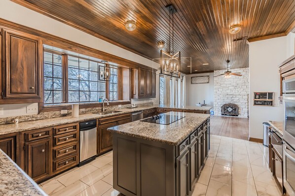 A spacious kitchen with granite countertops, wooden cabinets, a central island, and a stone fireplace. - Giant house near Frisco and Prosper (Prosper)