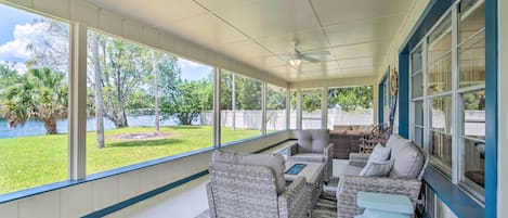 A covered patio with wicker furniture, large windows, and a view of a lake and trees.