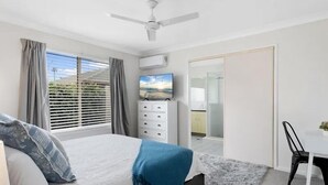 Une chambre à coucher avec un lit, une télévision, un ventilateur de plafond et une vue sur l’extérieur.