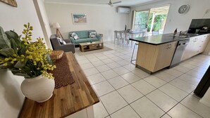 Une cuisine moderne avec un îlot central, un coin repas comprenant un canapé et une table basse, et un salon avec un divan et un tableau.