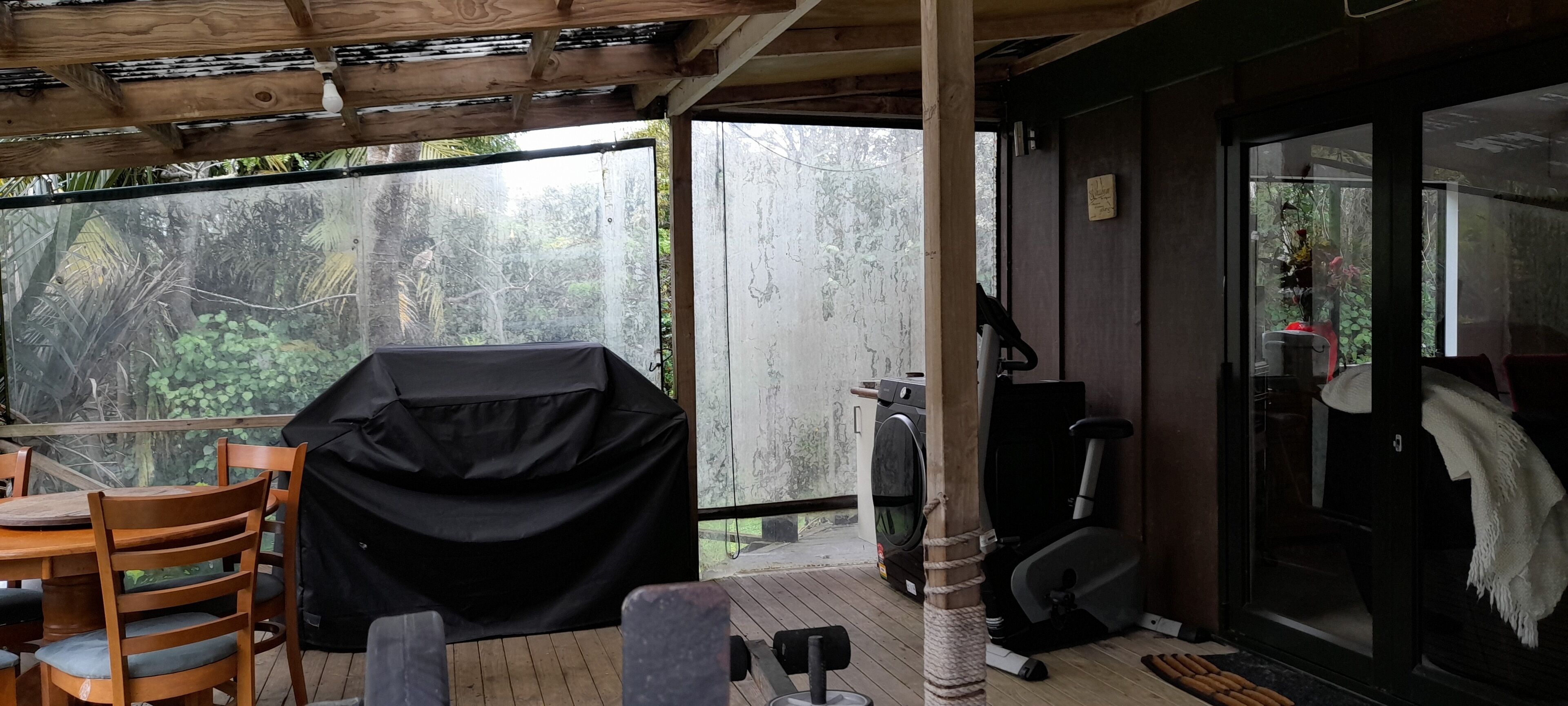 A covered outdoor area with a table and chairs, a covered grill, an exercise bike, and a stationary bike.