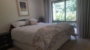 Un dormitorio con una cama grande, una mesita de noche, un ventilador y una ventana con cortinas.