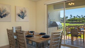 A dining area with a wooden table set for four, a grill, and a view of a golf course through a glass door. - Mauna Lani Townhome w/ Free Auberge Fitness Center Access (Kamuela)