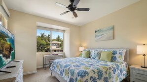 A bedroom with a bed, a desk, a chair, a ceiling fan, a window, and a painting on the wall. - Mauna Lani Townhome w/ Free Auberge Fitness Center Access (Kamuela)