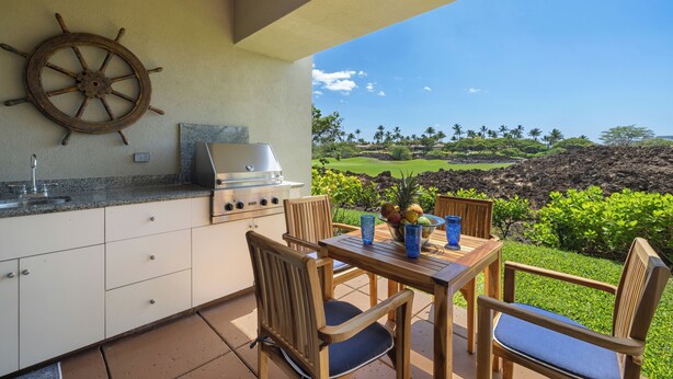 An outdoor kitchen with a grill, wooden chairs, and a view of a golf course. - Mauna Lani Townhome w/ Free Auberge Fitness Center Access (Kamuela)