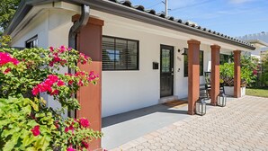 Una casa moderna con fachada blanca, una puerta negra y un porche cubierto con columnas de madera.