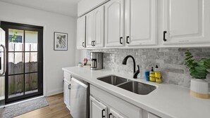 Una cocina moderna con gabinetes blancos, un lavamanos doble y un respaldo de azulejos.