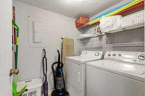 A laundry room with two washing machines, a dryer, a vacuum cleaner, and a mop.