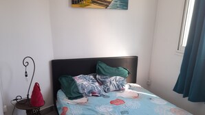 Ein Schlafzimmer mit einem Bett, einem Nachttisch, einer Wandlampe und einem Gemälde einer Strandansicht.