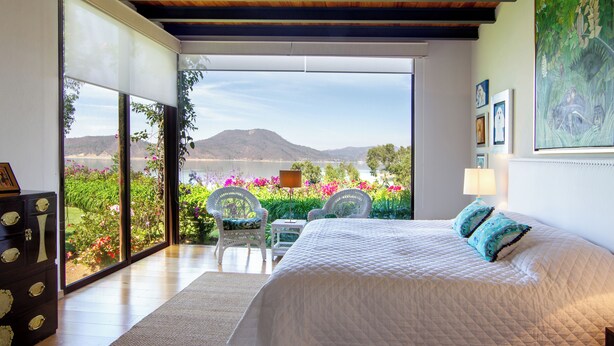 Un dormitorio con una cama grande, vistas a un jardín y montañas, y techo de madera.