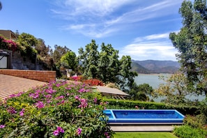 A swimming pool surrounded by lush greenery and a view of a lake.