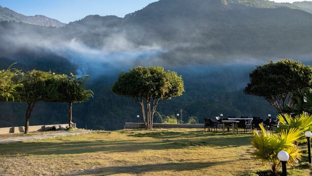 Un comedor con mesas y sillas, rodeado de árboles y un paisaje montañoso.