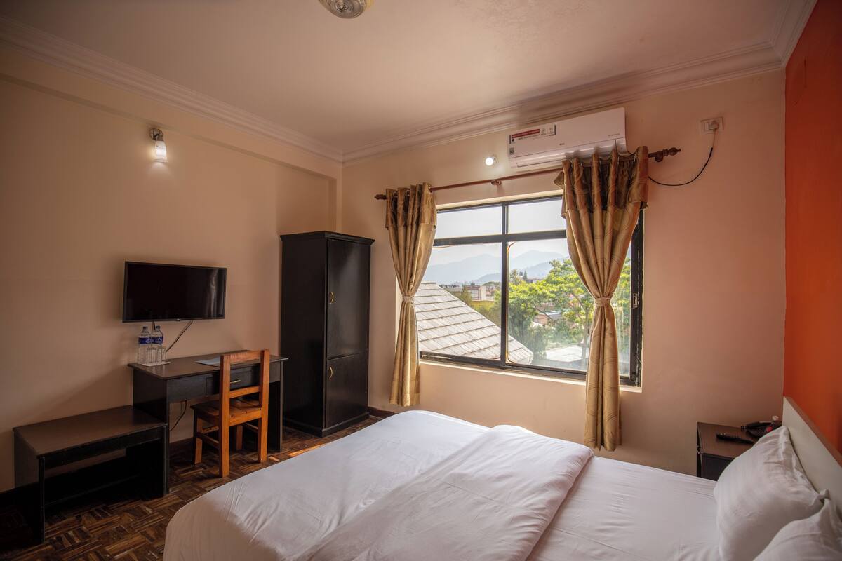 Ein Hotelzimmer mit Bett, Schreibtisch mit Stuhl, Fernseher und einem Fenster mit Vorhängen.