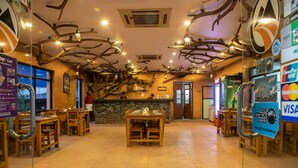 Un restaurante con mesas y sillas de madera, una pared de piedra y un techo con ramas de árboles.
