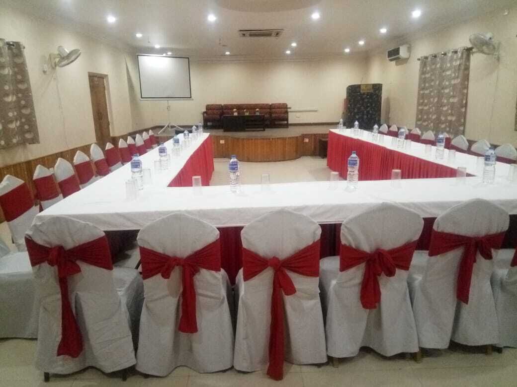 Un salón de conferencias con una larga mesa, sillas adornadas con cintas rojas y un escenario.