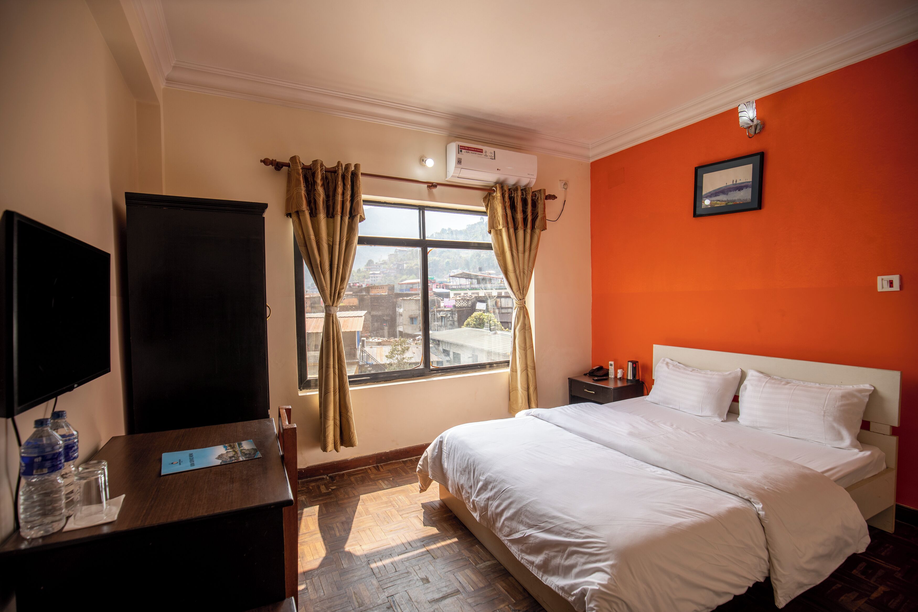 Habitación de hotel con cama, televisor, escritorio y botellas de agua, y ventana con cortinas.