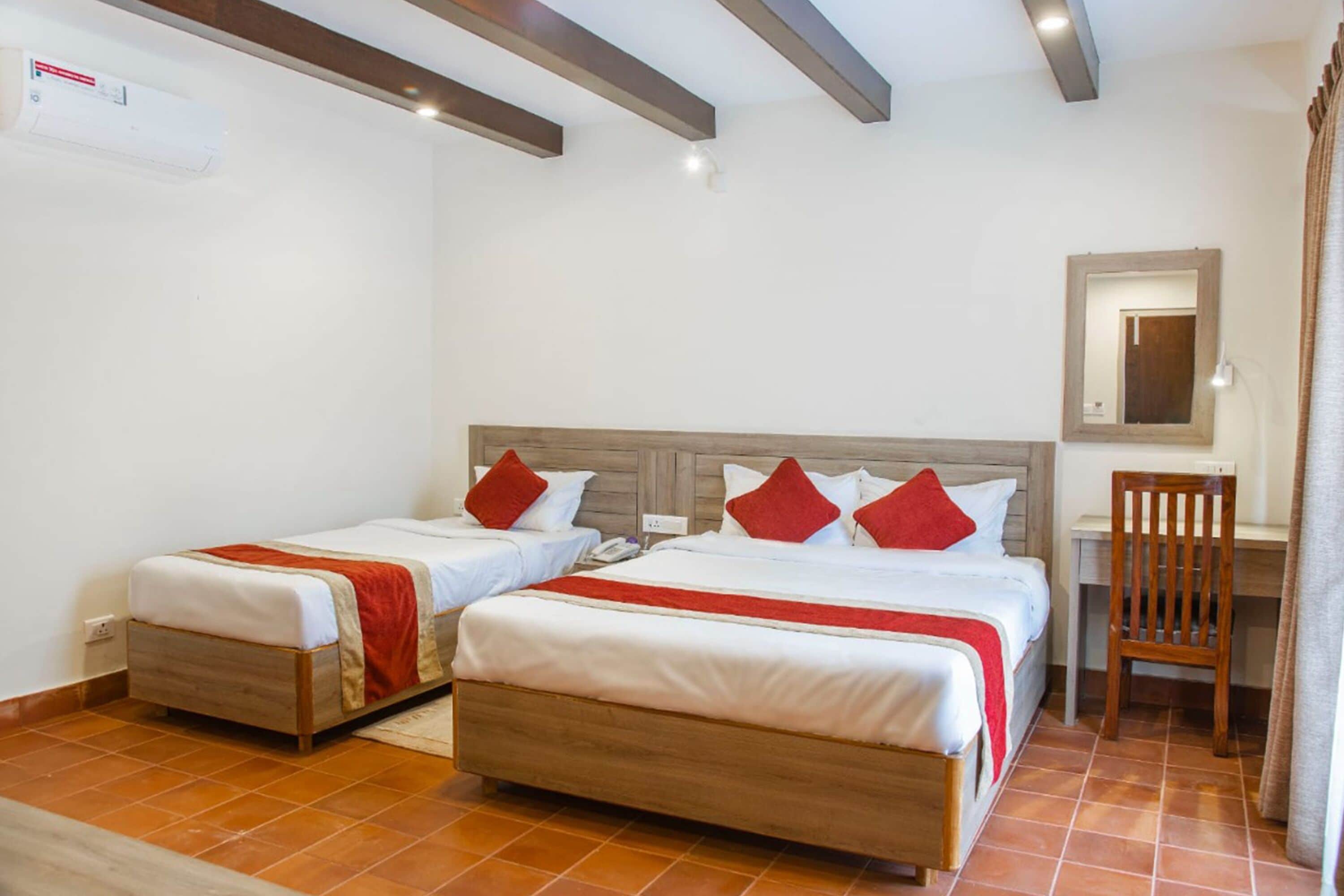 A hotel room with two single beds, a desk, a chair, and a mirror on the wall.