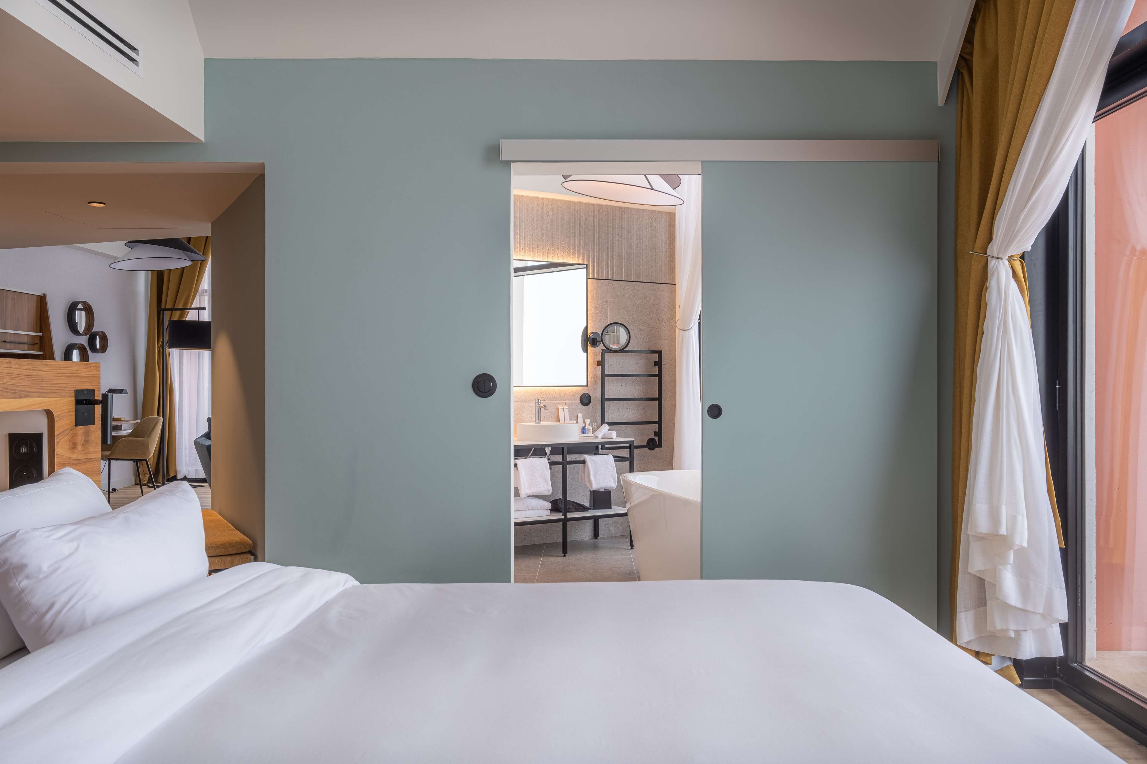 Habitación de hotel con una cama, un escritorio y un baño visible a través de una puerta abierta.