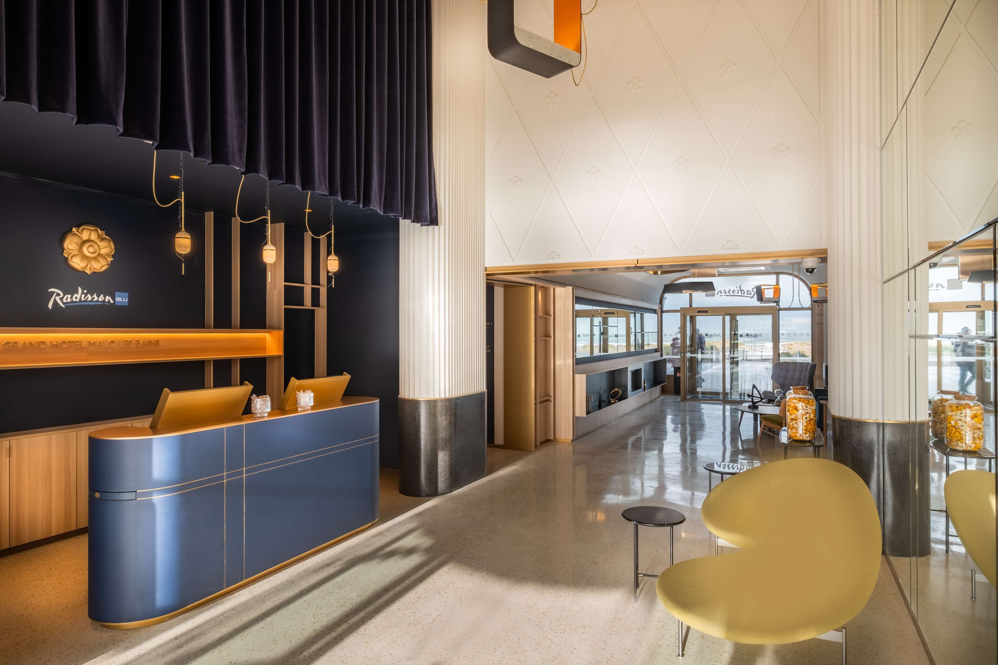 Ein moderner Hotel-Empfangsbereich mit einem blauen Empfangstresen und einer Sitzecke mit gelben Stühlen.