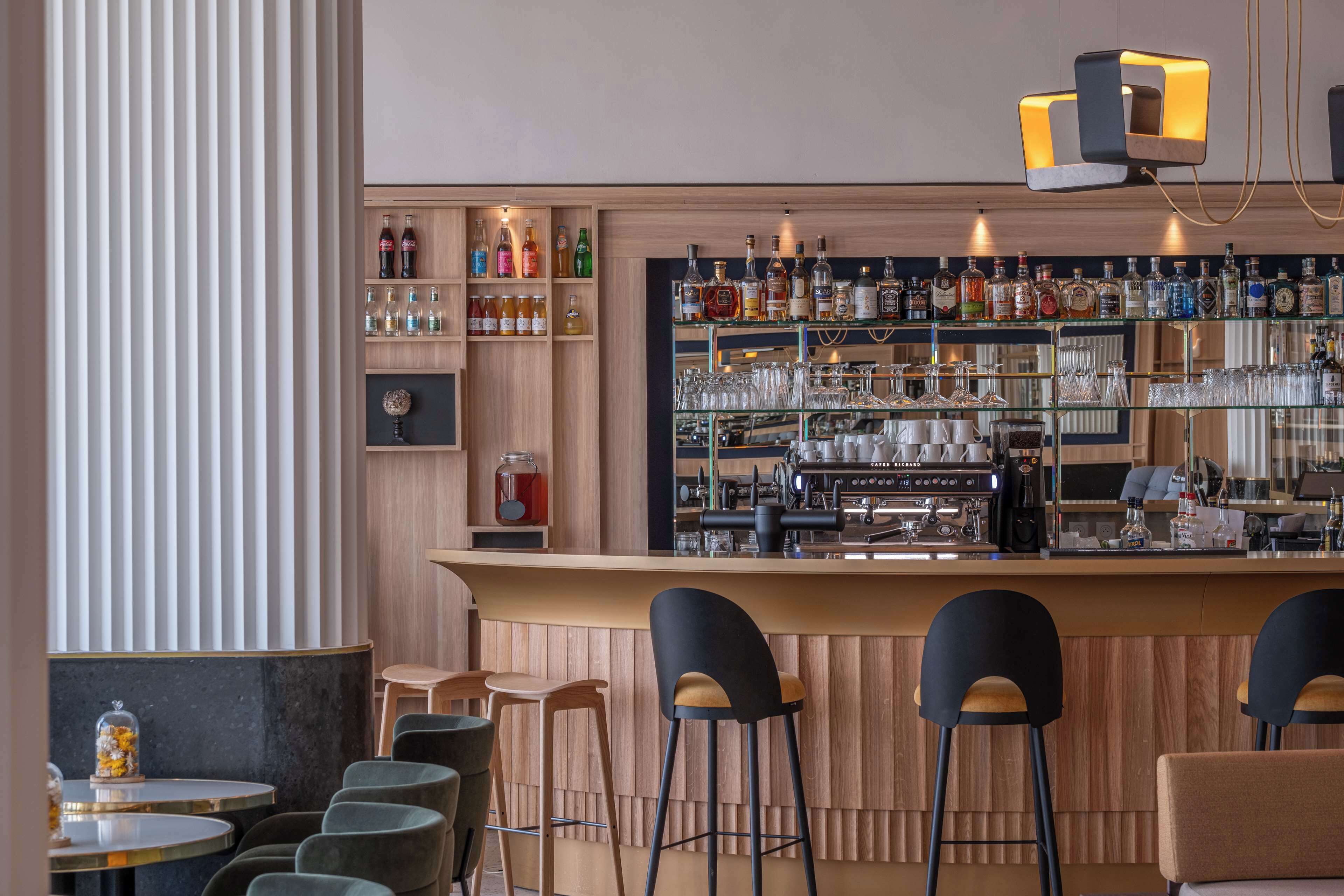 Un espace bar avec des étagères en bois remplies de bouteilles et de verres, un appareil à café et des tabourets de bar.