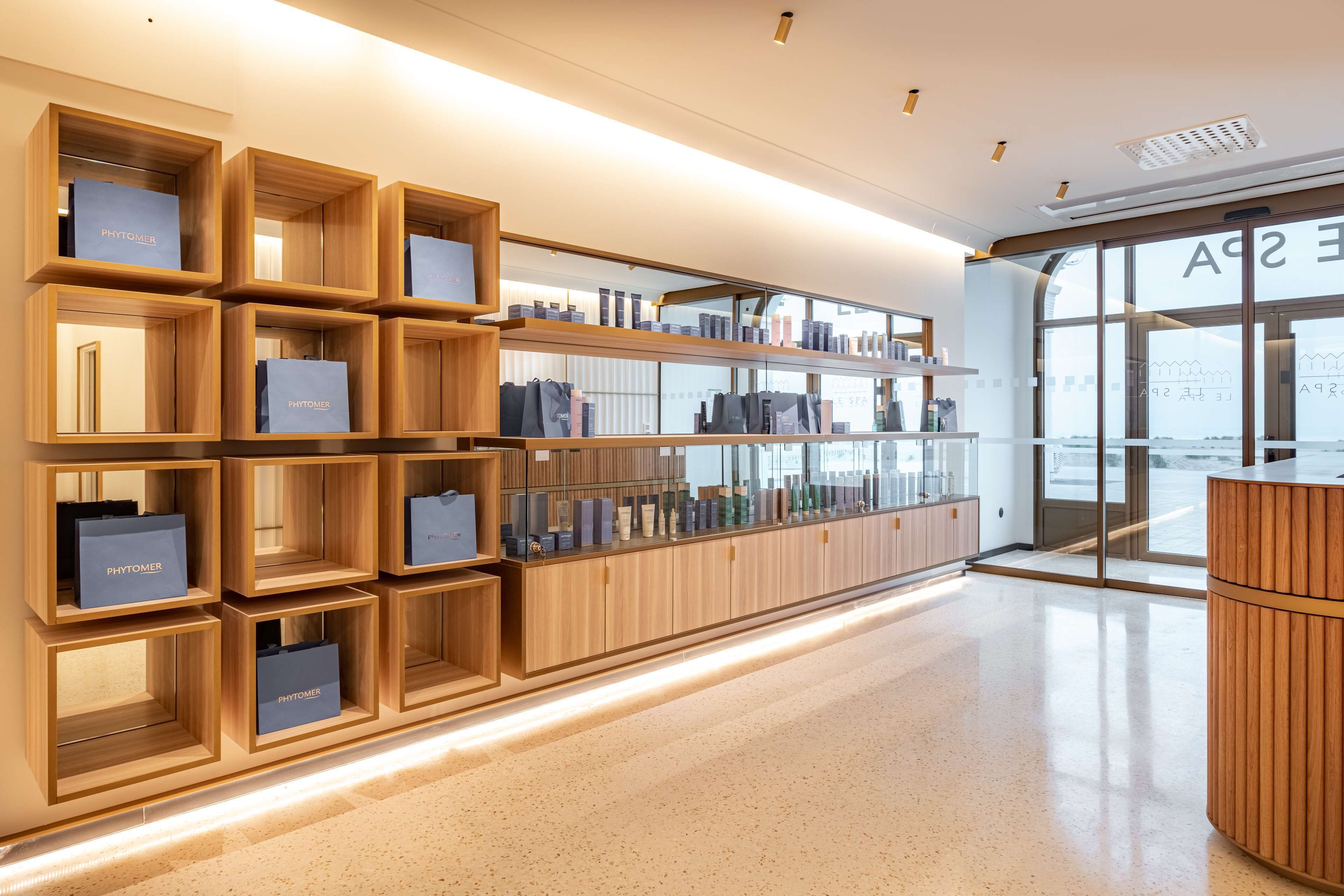 Un espace de vente moderne, doté d'étagères en bois où sont exposés les produits, et d'un espace d'accueil avec une porte en verre.