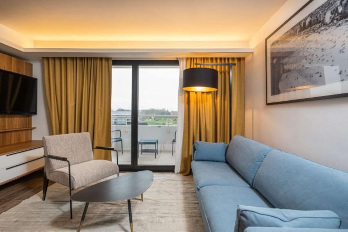 Ein modernes Hotelzimmer mit Sofa, Sessel und Flachbildfernseher.