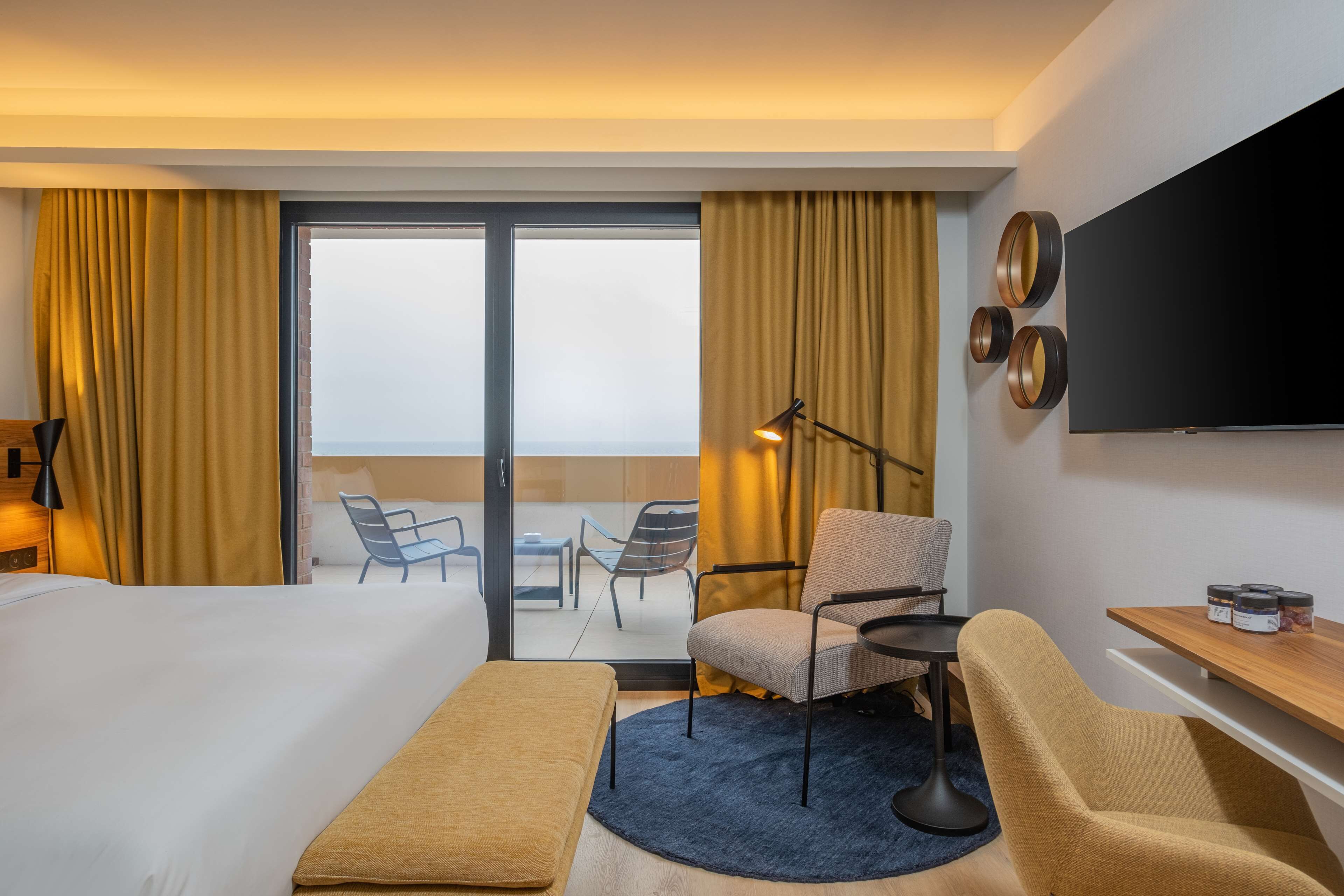 Habitación de hotel con cama, escritorio, silla, televisor y vistas al exterior.