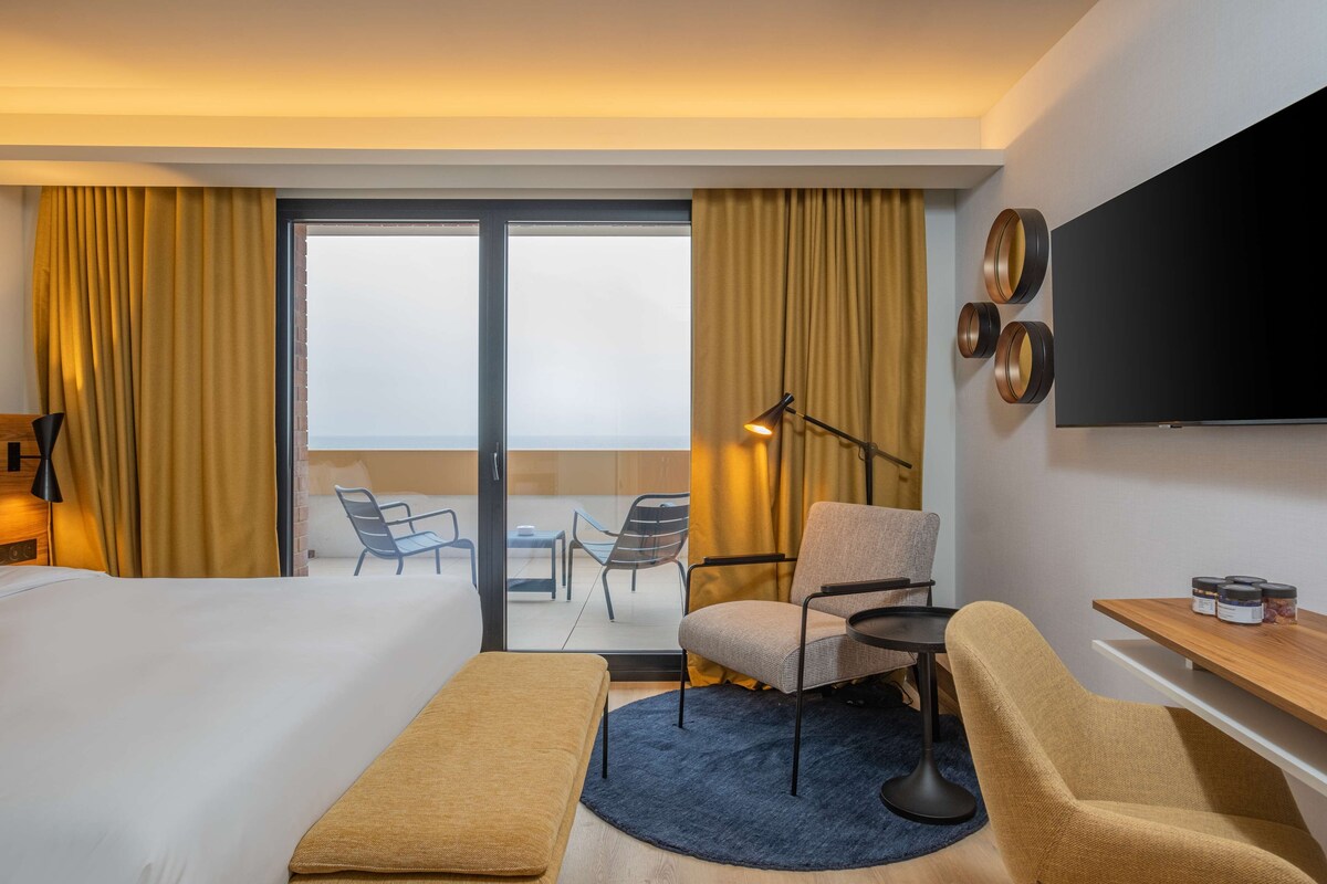 Een hotelkamer met een bed, een bureau, een stoel, een televisie en uitzicht op de omgeving.