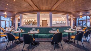 A modern restaurant with round tables, green cushioned seating, and a wooden ceiling.