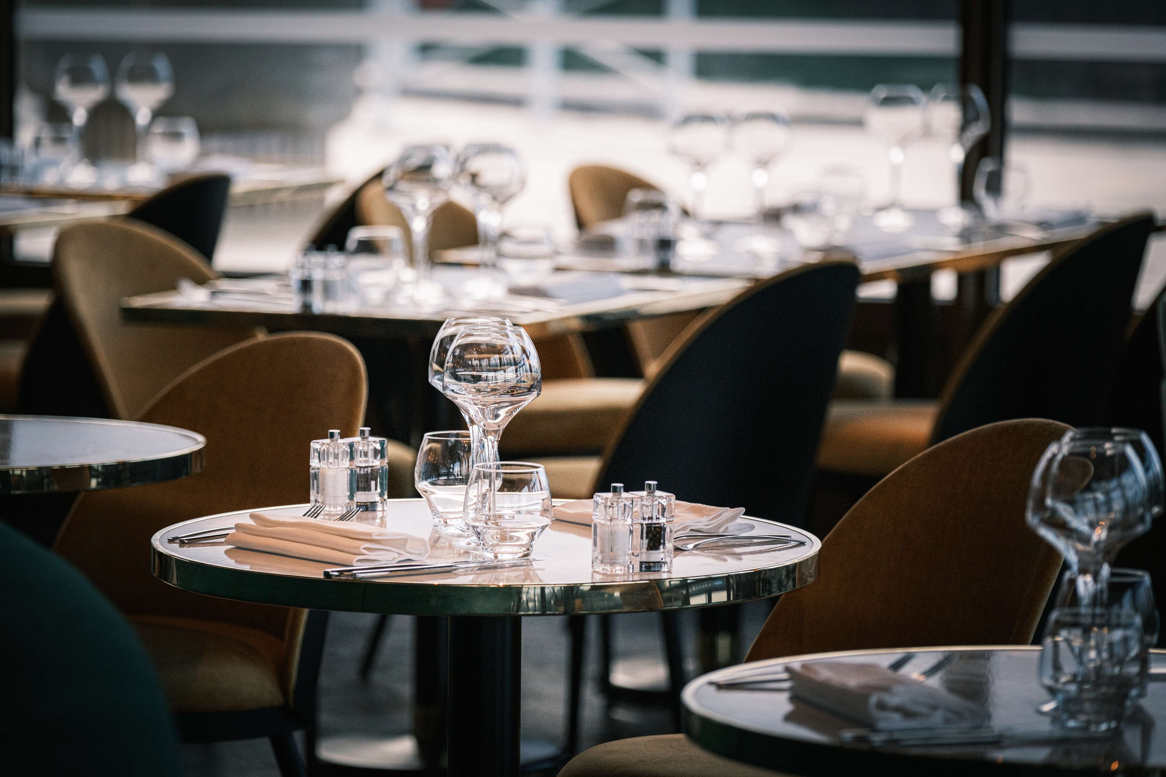 A restaurant with round tables set for dining, each with cutlery and glasses.