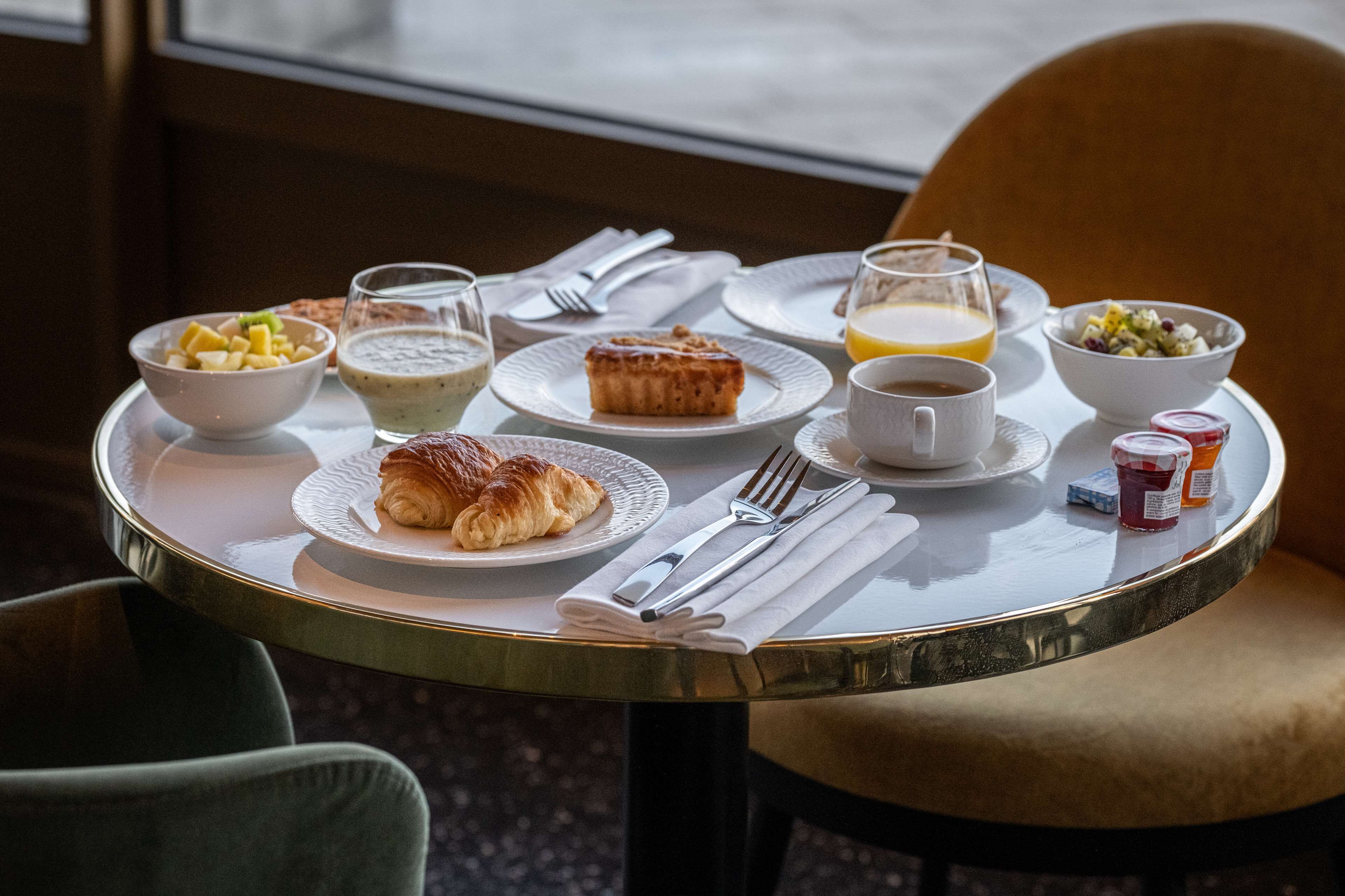 Una mesa de desayuno con cruasanes, fruta, cereal, jugo y café.