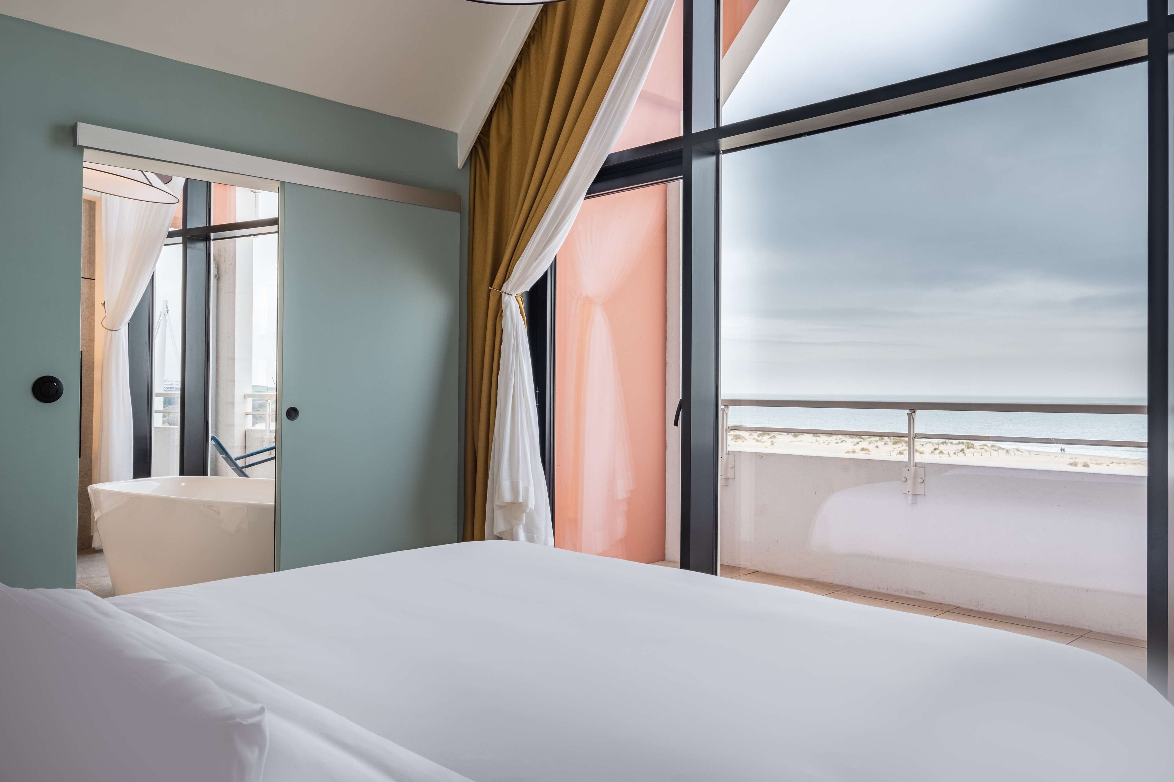 Une chambre d’hôtel avec un grand lit, une salle de bain avec baignoire et un balcon avec vue sur la plage.