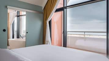 Habitación de hotel con una cama grande, baño con bañera y balcón con vista a la playa.