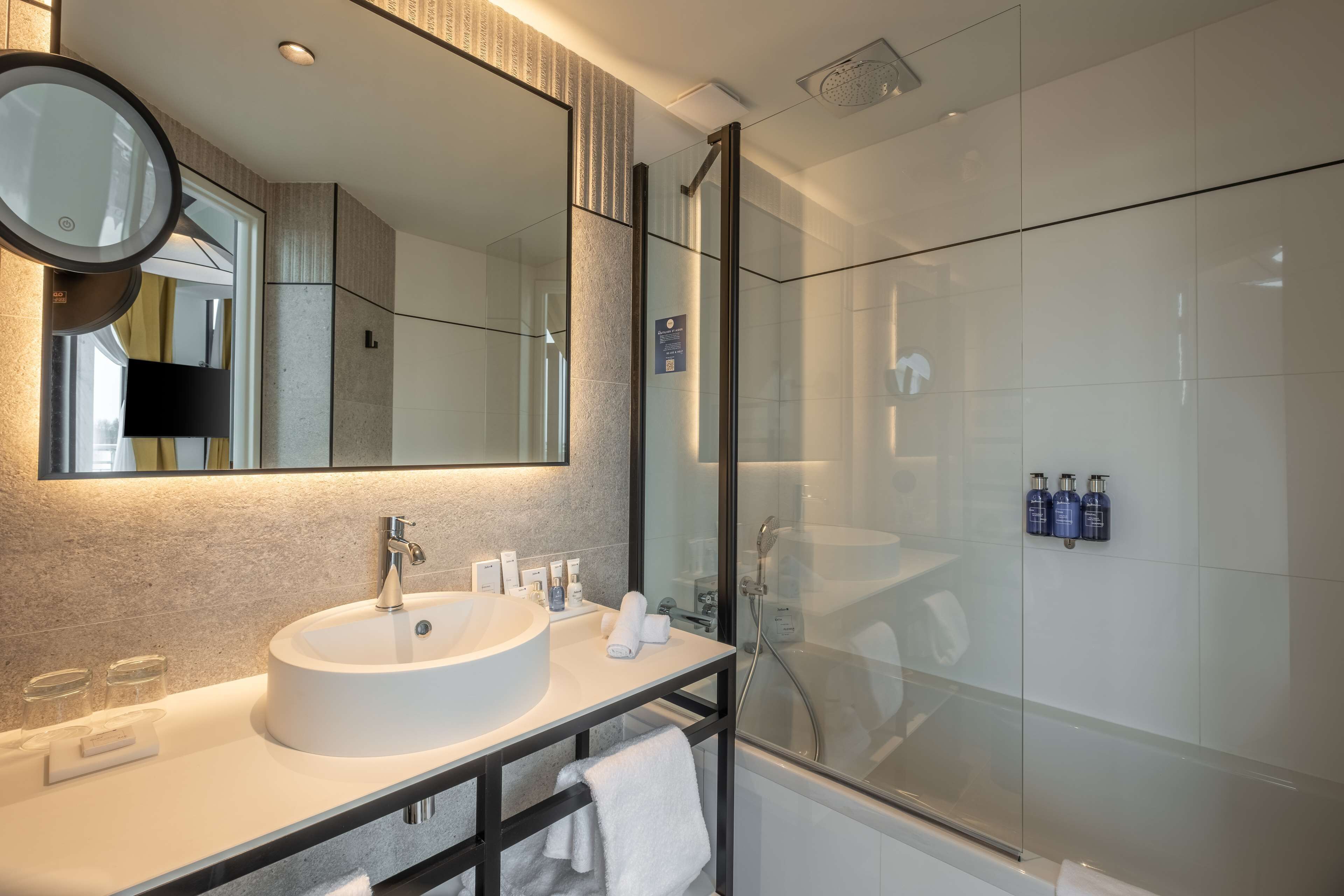 Une salle de bain moderne avec un grand miroir, un lavabo rond et une douche à parois de verre.