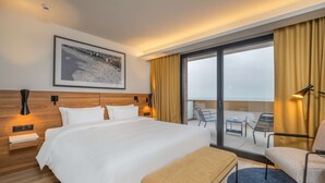A hotel room with a large bed, a bench, a chair, a desk, and a view of the sea through a sliding glass door. - Radisson Blu Grand Hotel & Spa, Malo-Les-Bains (Dunkirk)